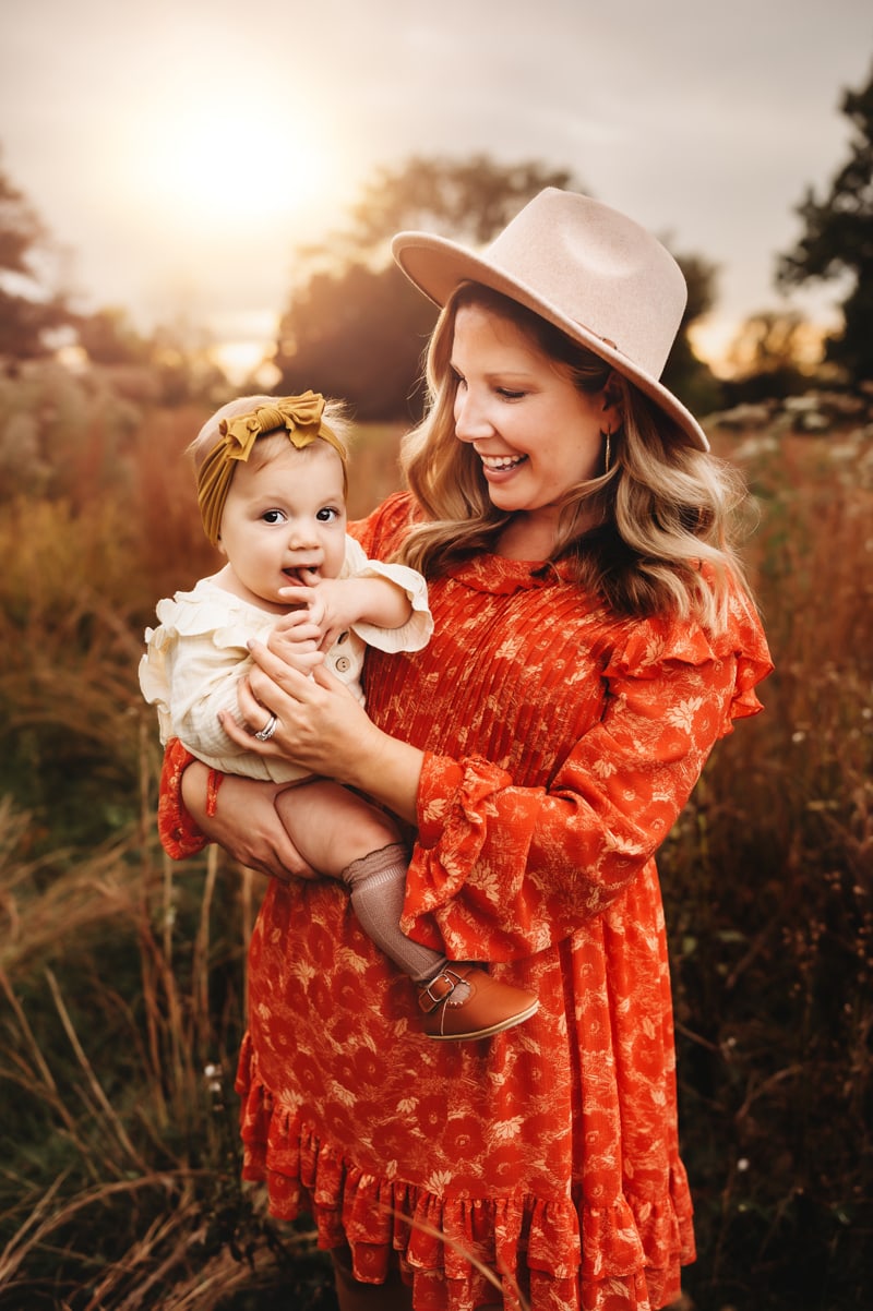 Mother holding a happy baby in a field at sunset